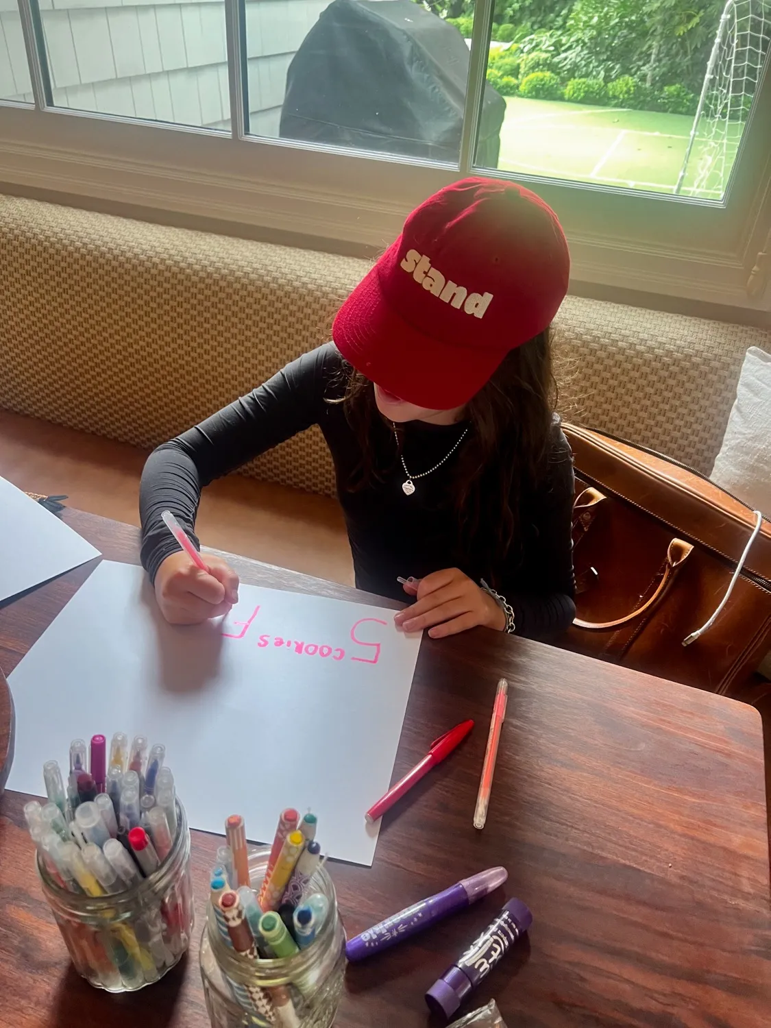 Stand kid drawing a Cookies $5 sign at a kitchen table